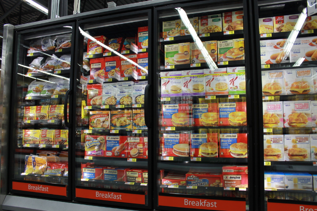 Lebensmittelpackungen, -deckel und -tüten sind in Schränken zu sehen, im Hintergrund ist ein beleuchtetes Dach zu erkennen, möglicherweise in einem Geschäft.