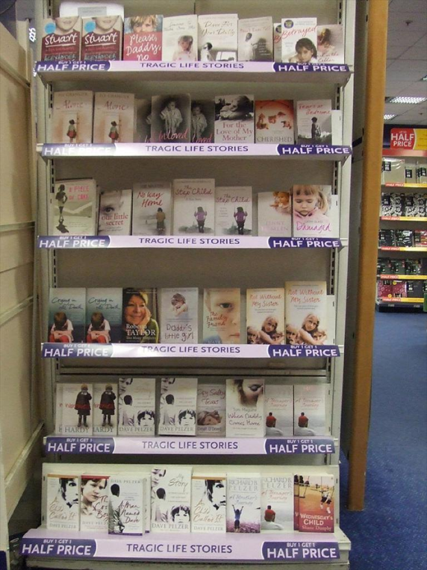 Eine Innenansicht, die ein Bücherregal mit vielen Büchern, eine Tür auf der linken Seite, ein weiteres Regal im Hintergrund mit ein paar Gegenständen und Lampen an der Decke zeigt.