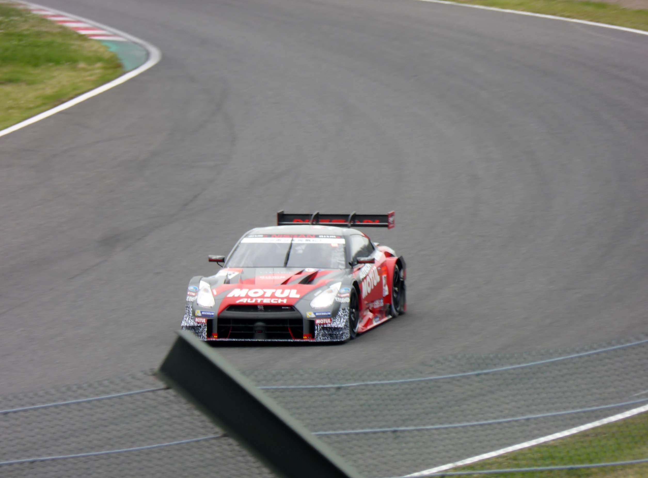 Ein Nissan GT-R Nismo GT3 Rennauto auf der Nürburgring 24 Stunden Rennstrecke, mit grünem Gras auf beiden Seiten des Asphalts.