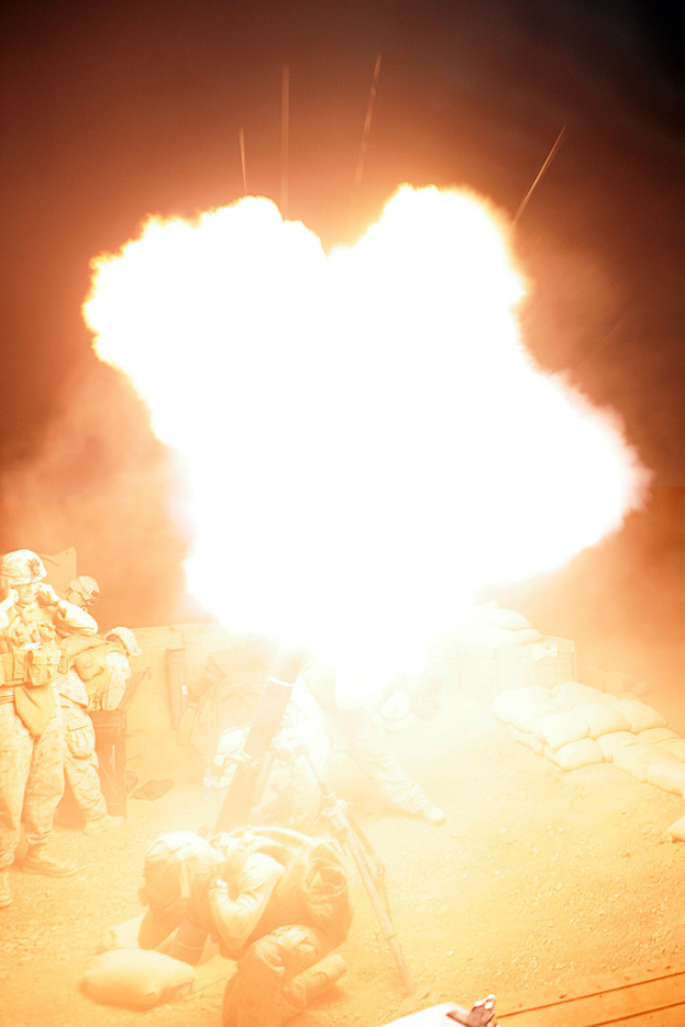 Mehrere Personen in Uniform und Helm auf einem Gelände mit einigen Taschen drumherum, in der Mitte brennt ein Feuer.
