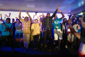 Ein Schwarz-Weiß-Foto eines Paares, das auf einer Bühne tanzt, mit ein paar Leuten auf einer Treppe im Hintergrund und einem Pfahl im Vordergrund.