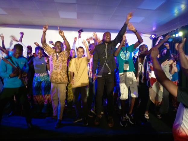 Ein Schwarz-Weiß-Foto eines Paares, das auf einer Bühne tanzt, mit ein paar Leuten auf einer Treppe im Hintergrund und einem Pfahl im Vordergrund.