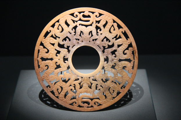 Ein chinesischer geschnitzter Jade-Teller in einem Museum ausgestellt, mit detaillierten Gravuren auf seiner Oberfläche vor einem dunklen Hintergrund.