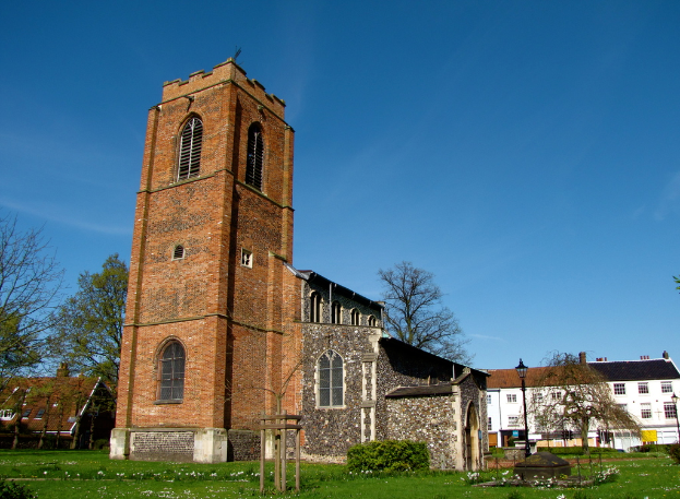 Eine grüne Fläche mit einem Mast, Gebäuden und Bäumen im Hintergrund.