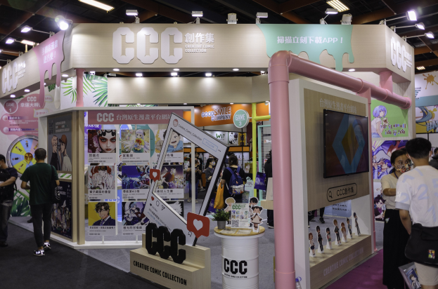 Gruppe von Menschen vor einem Messestand mit Werbetafeln, Fernseher und Deckenbeleuchtung, wahrscheinlich mit einer kreativen Comic-Sammlung.