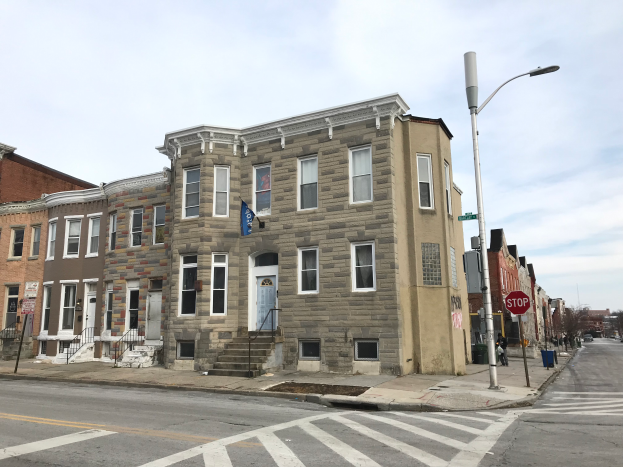 Eine Reihe neuer Häuser an einer Straßenecke in Philadelphia, mit Fahrzeugen, Laternenmasten, Schildern und Bäumen im Hintergrund unter einem bewölkten Himmel.