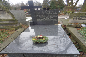 Ein Friedhof mit einem zentralen Grabstein, der mit einem Kranz geschmückt ist und von Bäumen umgeben ist.