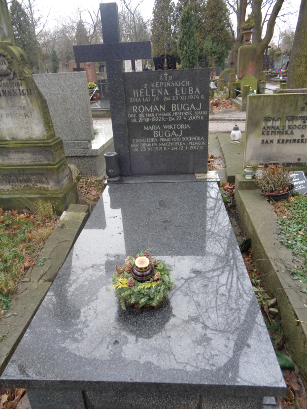 Ein Friedhof mit einem zentralen Grabstein, der mit einem Kranz geschmückt ist und von Bäumen umgeben ist.