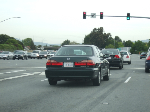 Eine vielbefahrene Straße mit mehreren Fahrzeugen, drei Strommasten und einer Ampel auf der rechten Seite bei klarem Himmel.