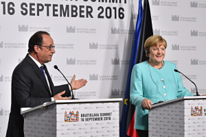 Bundeskanzlerin Angela Merkel und Frankreichs Präsident François Hollande stehen vor zwei Podien mit Mikrofonen, beide lächeln, mit einem Banner "Bratislava-Gipfel 2016" im Hintergrund.