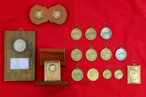 Sammlung von Medaillen auf rotem Tuch mit einem hölzernen Schild oder Preis in der Mitte.