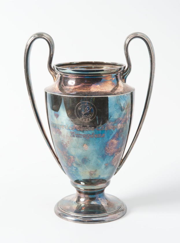 Der UEFA-Champions-League-Pokal, eine stählerne Tasse mit zwei Griffen und einem blauen und silbernen Farbschema, beschriftet mit "UEFA Champions League", vor einem weißen Hintergrund dargestellt.
