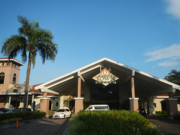 Der Eingang eines Resorts mit Palmen vorne, umgeben von Gebäuden, Fahrzeugen auf der Straße, Verkehrshütchen, Büschen, Bäumen und einem bewölkten Himmel im Hintergrund.