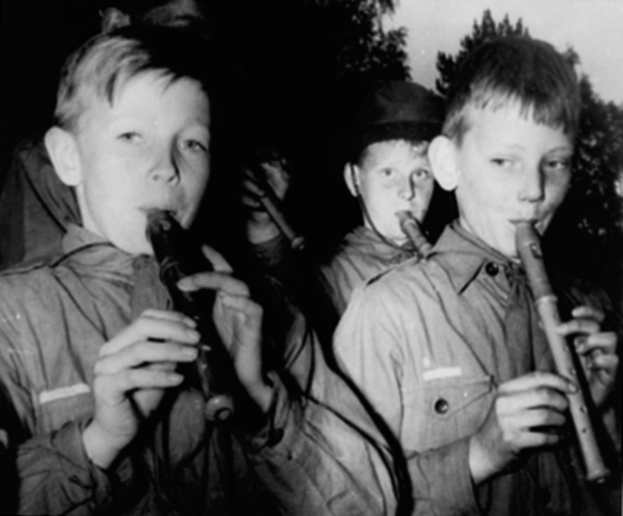 Eine Gruppe junger Jungs, die Flöten im Freien spielen, mit Bäumen im Hintergrund in einem Schwarz-Weiß-Bild.