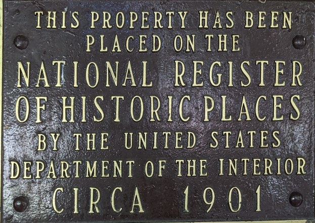 Eine Metalltafel an einem Gebäude trägt die Aufschrift "Dieses Gebäude steht unter Denkmalschutz".