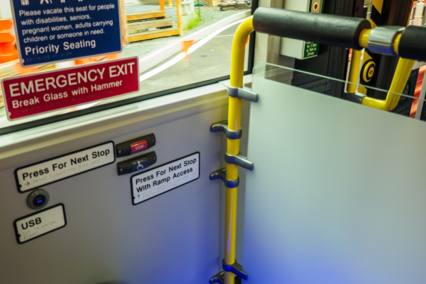 Notausgangsschild an der Seite eines Zuges, das eine Tür, einen Griff und ein Glasfenster zeigt, durch das man eine Straße, Pfosten und andere Gegenstände im Freien sehen kann.