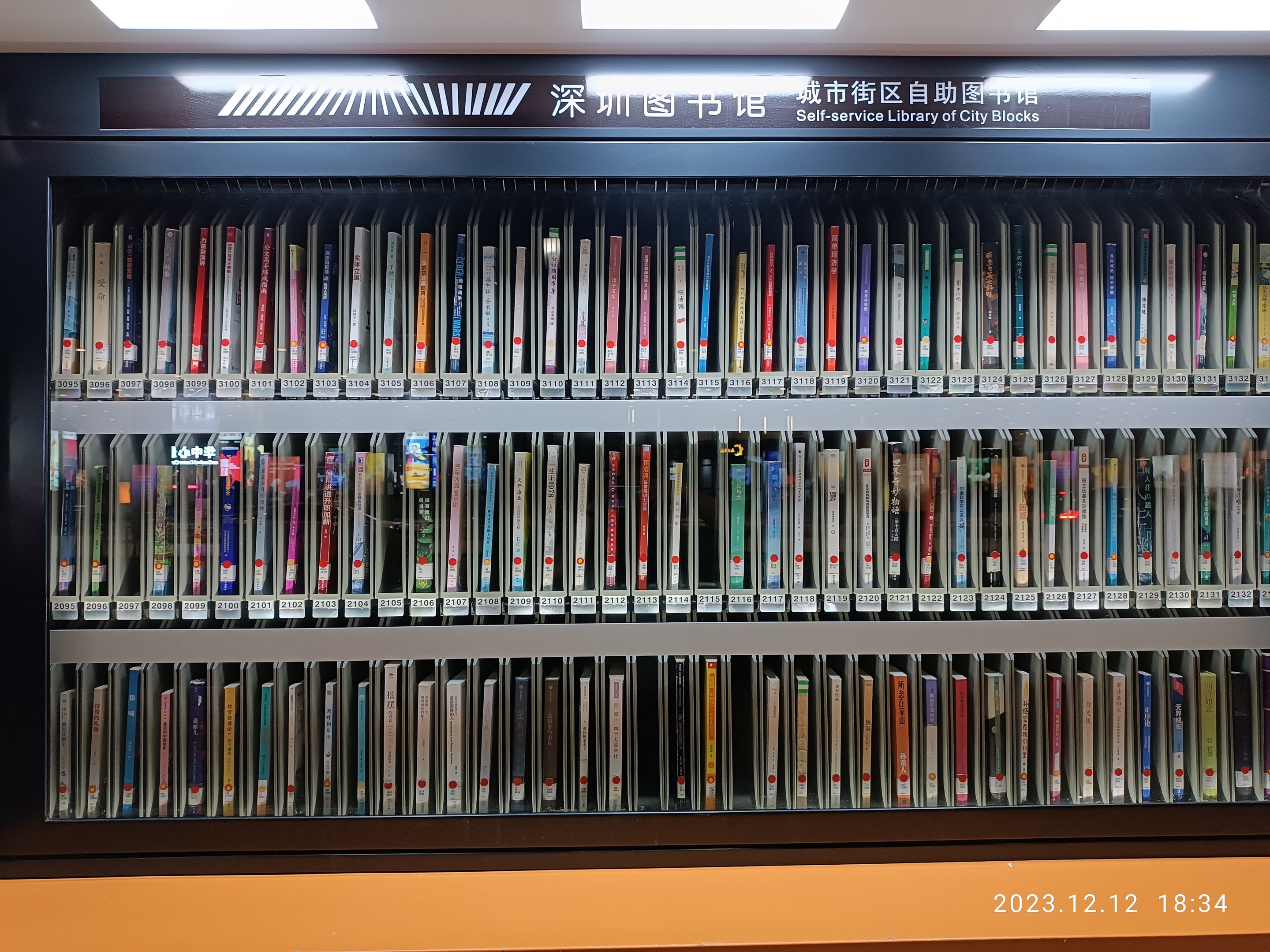 Eine gut beleuchtete Bibliothek mit Reihen von Bücherregalen, einem sichtbaren Informationsschild und einem Wasserzeichen unten, das an eine Selbstbedienungsbibliothek der Stadtblocks erinnert.