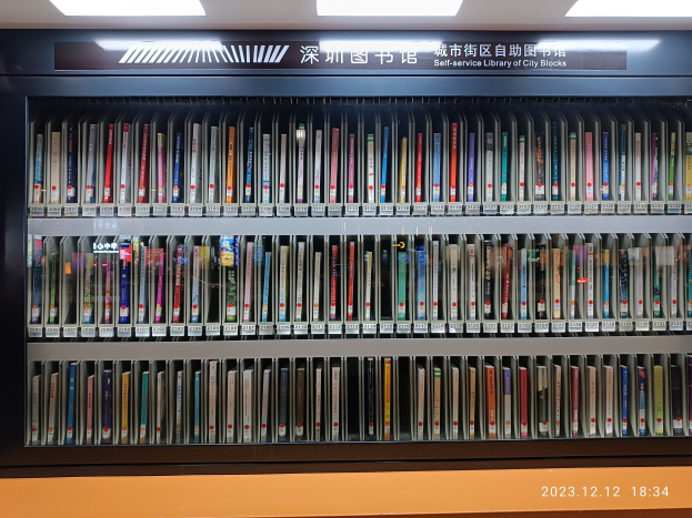 Eine gut beleuchtete Bibliothek mit Reihen von Bücherregalen, einem sichtbaren Informationsschild und einem Wasserzeichen unten, das an eine Selbstbedienungsbibliothek der Stadtblocks erinnert.