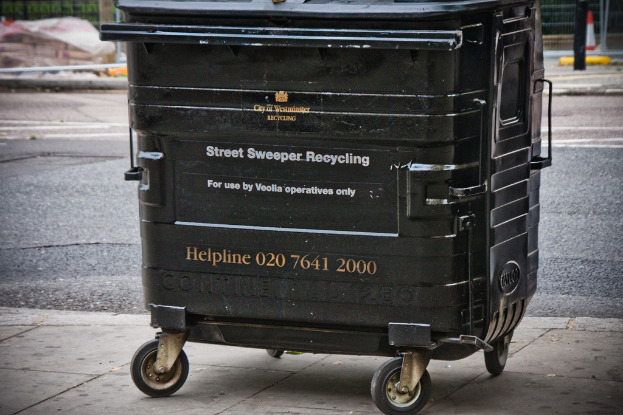 Ein schwarzer Mülltonnen ist in der Mitte des Bildes mit einer Straße unten.