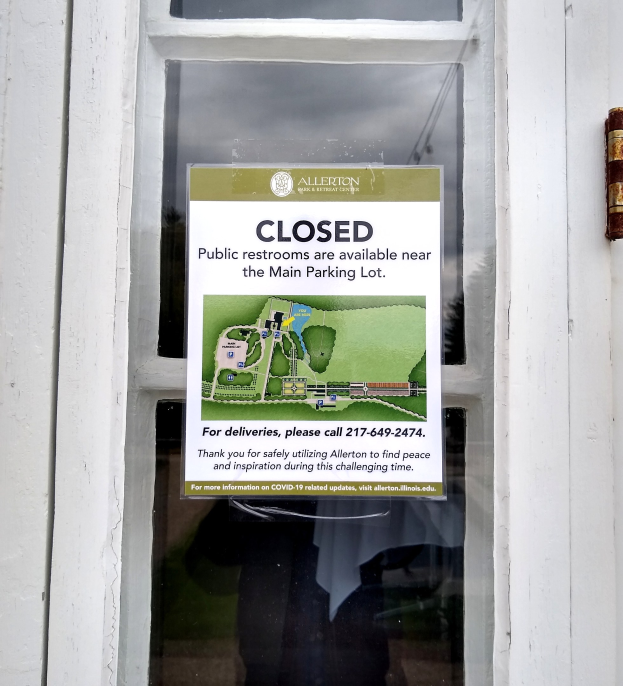 Glasstür mit einem Schild, auf dem "Geschlossene öffentliche Toiletten in der Nähe des Hauptparkplatzes" steht und ein undeutliches Objekt auf der rechten Seite.