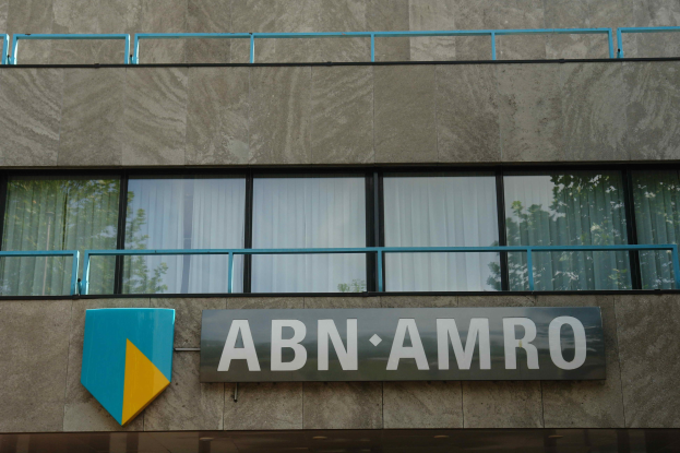 Außenansicht eines ABN AMRO-Gebäudes mit einem Schild, einer Tafel, die es als Hauptsitz angibt, Geländern und Vorhangglasfenstern, in Bezug auf eine 1,5 Milliarden EU-Strafe.