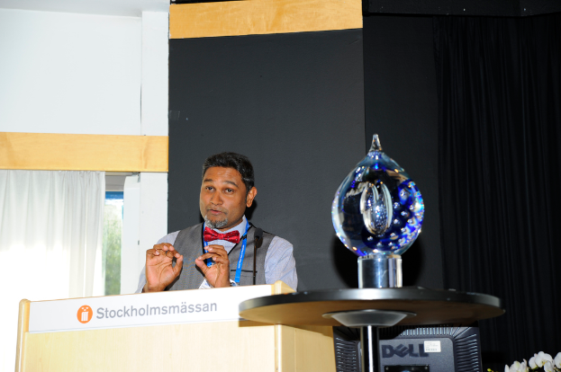 Ein Mann steht neben einem Podium und spricht mit einer Wand dahinter.