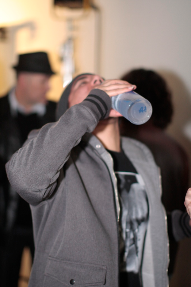 Ein Mann in der Mitte des Bildes hält eine Flasche und trinkt Wasser, umgeben von ein paar anderen Menschen.