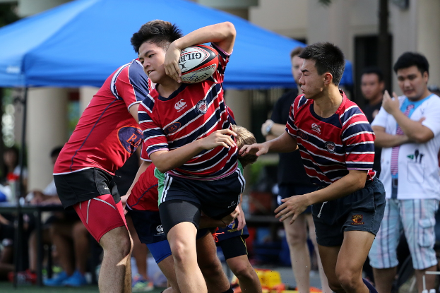 Eine Gruppe von Menschen, die Outdoor ein Spiel spielen, mit einem Jungen in der Mitte, der einen Ball hÃ¤lt, wÃ¤hrend andere stehen und im Hintergrund zuschauen, nÃ¤he eines blauen Zeltes.