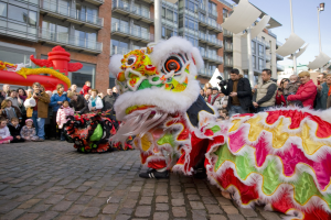 Eine Löwen-Tanzvorstellung während einer Chinesischen Neujahrsfeier in Amsterdam, mit einer Zuschauermenge und Gebäuden im Hintergrund.