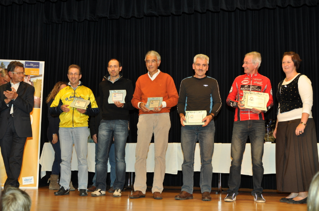 Eine Gruppe von Menschen steht auf einer Bühne und hält Zertifikate in den Händen, im Hintergrund eine Fahne, ein Tisch zur Seite und ein schwarzer Vorhang.