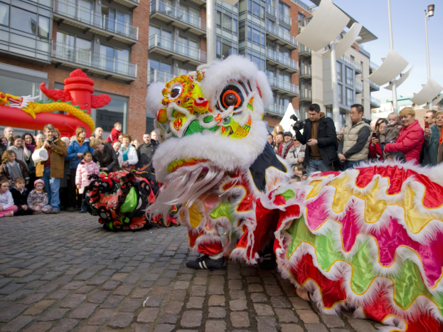 Tanz der Löwen bei einer Chinesischen Neujahrsfeier in Amsterdam, mit einer Zuschauermenge und Gebäuden im Hintergrund.