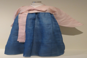 Eine Schaufensterpuppe in einem blauen und pinken Hanbok mit detaillierten Mustern, die vor einer neutralen Wand in einem Museum ausgestellt ist.