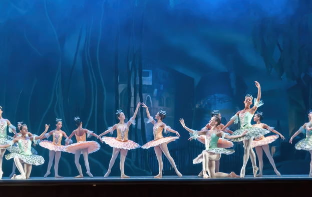 Eine Gruppe von Balletttänzerinnen in farbenfrohen Kostümen performs *Der Nussknacker* auf der Bühne der Royal Opera House, bewegend sich in synchronisierter Anmut gegen einen blauen Hintergrund.