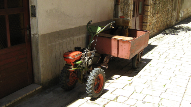 Ein Zugfahrzeug mit einem Anhänger auf einer Straße, neben einem Haus mit sichtbaren Türen.