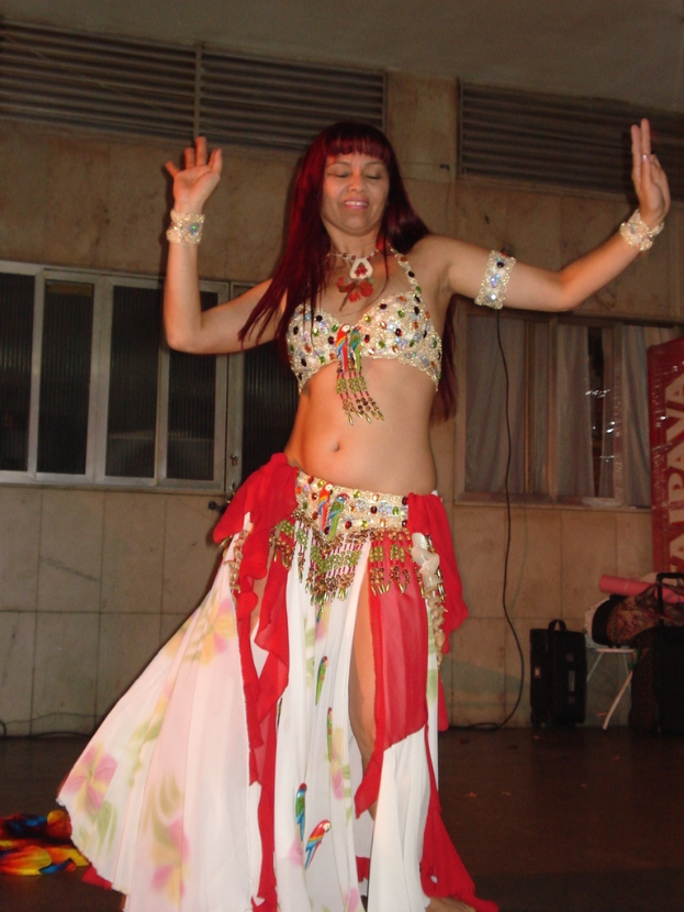 Eine Frau in einem Kleid führt einen Bauchtanz auf, wobei Fenster im Hintergrund zu sehen sind.