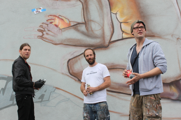 Menschen mit Farbsprühdosen in der Hand, mit Graffiti an der Wand dahinter.