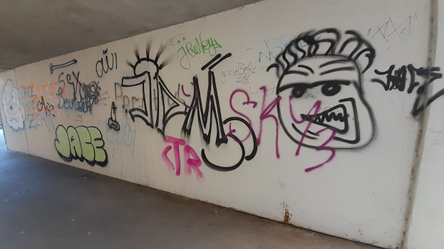 Eine Wand in einer Tiefgarage voller bunter, lebendiger Graffiti mit einer Decke oben drauf.